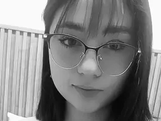 eve_aura poses for a close-up selfie, showing her face and dark hair with bangs while wearing thin-rimmed glasses.