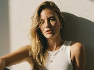 gentlebreeze poses with her long blonde hair and bare shoulders against a plain white wall in soft lighting.