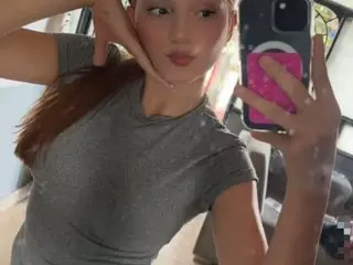 golden_princess_ggh poses in a tight grey t-shirt, showing her long brown hair and face in a mirror selfie.
