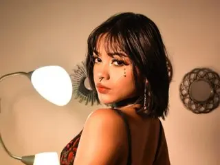 hannaferratti poses with a direct gaze, showing her dark hair and shoulders against a warm, lit background.