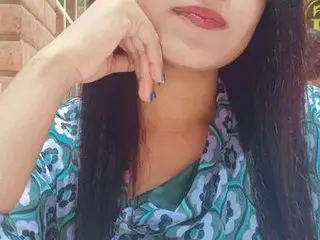 Young woman in a teal patterned blouse posing thoughtfully outdoors against a brick wall.