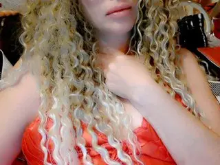 Woman with long blonde curly hair wearing a red satin dress in a soft indoor setting.