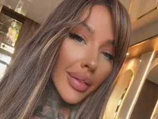 Beautiful woman with long highlighted hair and glamorous makeup smiling in a luxury gold interior.