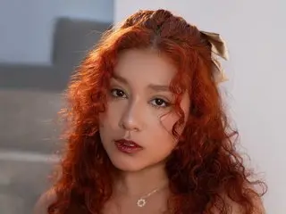 Young woman with curly red hair and natural makeup posing in a bright indoor setting.