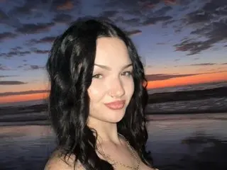 Smiling woman with wavy black hair wearing a gold necklace at a sunset beach.