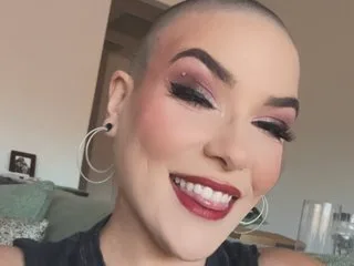 jaynewoods smiles with a close-up view of her face, showing her dark eyebrows, heavy eye makeup, and red lipstick.