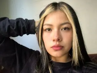 Young woman with blonde face-framing highlights wearing a black sweatshirt in a soft indoor setting.