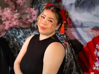 katheringoezz69 poses with her blonde hair styled up, wearing a black sleeveless top against a decorative floral and patterned background.