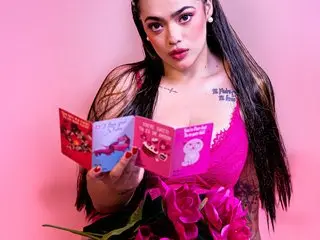 kayllaEvanss poses in a pink bra, showing her cleavage and long dark hair against a pink background.