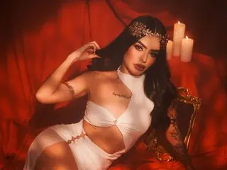 kendallSiilver poses in a white bra and matching undies, showing off her cleavage and long dark hair against a red background.