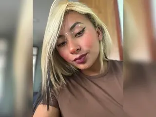 khalessyJ with long blonde hair, wearing a brown t-shirt and looking directly at the camera.