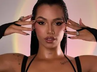 kloewatson19 poses with her hands framing her face, showing her dark hair and clear skin against a soft purple background.