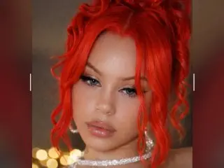 Young woman with vibrant red wavy hair and glamorous makeup wearing a sparkling silver necklace.