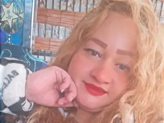 l_ambar33 poses with her hand near her face, showing her blonde hair and red lipstick in a close-up shot.