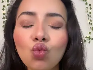 Young woman with glamorous pink makeup and closed eyes making a playful kissy face in front of ivy decor.