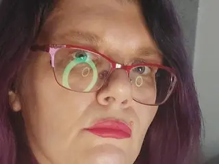 leeanneHill looks at the camera with her dark hair and red glasses, showing her face and red lipstick.