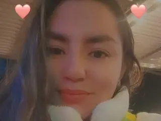 lexxyy24 looks directly at the camera with long dark hair and a soft smile, wearing a white fuzzy top or scarf.