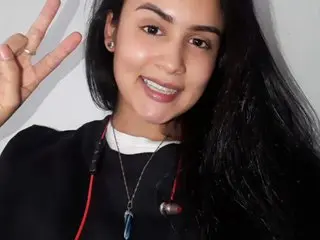 lilith_zaffron smiles while posing with a peace sign, showing her long black hair and wearing a black top.