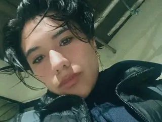 Young woman with wavy dark hair wearing a black puffer jacket in a moody, low-angle indoor setting.