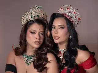Two glamorous beauty queens in sparkling crowns and emerald jewelry posing for a luxury portrait.