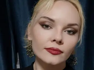 liquedlove poses with a close-up headshot, showing her blonde hair and red lipstick against a dark blue background.