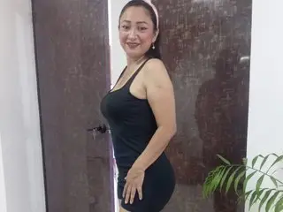 Smiling woman in a black sleeveless dress standing in a modern room with dark wood doors.