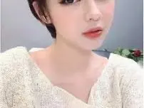 lisarose_28x poses close-up, showing her face, dark hair, and a white knit top against a plain background.