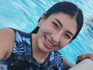 Lissawhatson smiles while posing in a blue patterned top, with her wet hair and face visible against a blue swimming pool background.