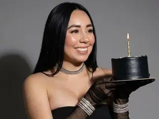 lopezariana smiles while holding a black birthday cake with a single lit candle, wearing a silver choker and black strapless top.