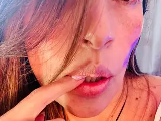 lourreinStounn licks her lips while running a finger over her mouth, showing her face and long brown hair.