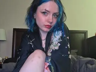 m0thra poses with a direct gaze, wearing a black floral print shirt that hangs open over her shoulders.