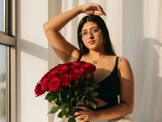 megann_up wears glasses and a black tank top while holding a large bouquet of red roses in front of a window.