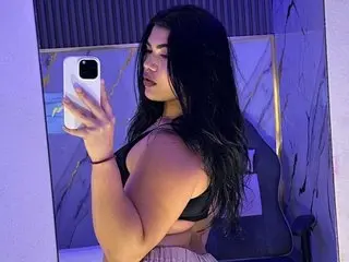 melanyrouse24 poses with her long dark hair, wearing a black bra or top while looking at her phone in a mirror.