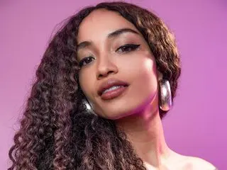 Beautiful woman with curly hair and silver hoop earrings posing against a vibrant pink background.