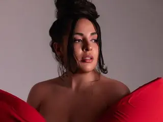 Glamorous woman with dark updo and makeup posing in red satin fabric against a neutral studio background.