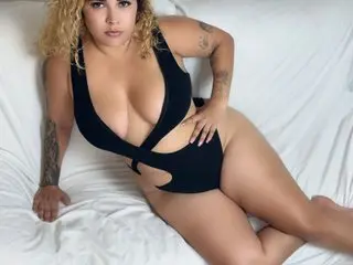 miasexxxydoll is a blonde woman in a black bodysuit laying on a white bed.