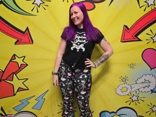 missgennyrock poses with her hands on her hips, wearing a black t-shirt and patterned leggings, with her long purple hair down against a bright yellow background.