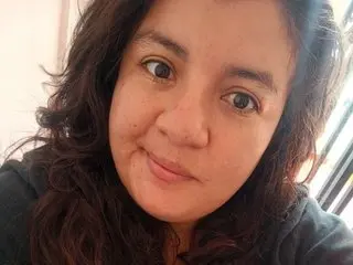 mystery_pisque looks directly at the camera with a slight smile, showing her face and dark wavy hair in a close-up shot.