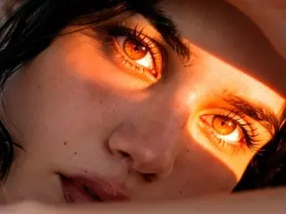 natashaajackson looks directly into the camera with a close-up view of her eyes and face, lit by warm, orange-toned light.