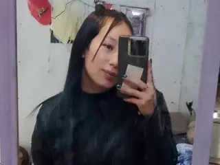 Young woman with long black hair taking a mirror selfie in a casual indoor setting.