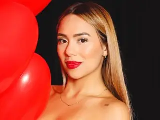 Glamorous woman with blonde hair and red lipstick posing with bright red balloons against a black background.