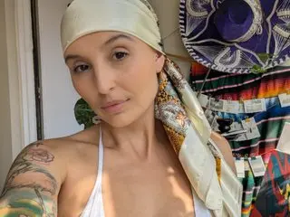 oh_charlie poses with a white headwrap, showing her bare shoulders and chest in a white top against a colorful patterned background.