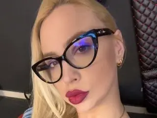 Blonde woman with red lipstick and black cat-eye glasses posing for a stylish close-up portrait.