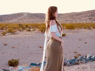 Bohemian woman in a white lace top and olive maxi skirt standing in a desert landscape at sunset.