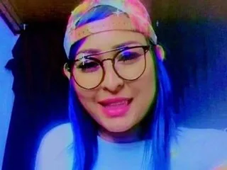 pamelasam wears a colorful patterned hat and black glasses while smiling at the camera.