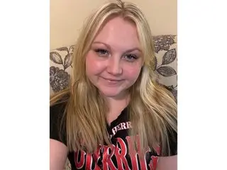 phatassblonde, a blonde woman, looks at the camera while wearing a black t-shirt in a close-up shot.