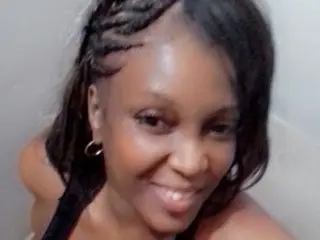 plentyfu smiles while showing her dark hair styled in thin braids, looking directly at the camera in a close-up shot.