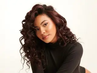 saamara poses with her long, wavy dark hair, wearing a black turtleneck against a plain white background.