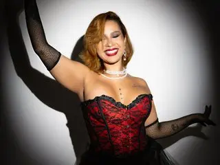 Smiling woman in red lace corset and black mesh gloves posing joyfully against a studio backdrop.