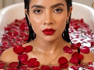 sarahbigboob with long dark hair and red lipstick, posing naked in a white bathtub filled with red rose petals.